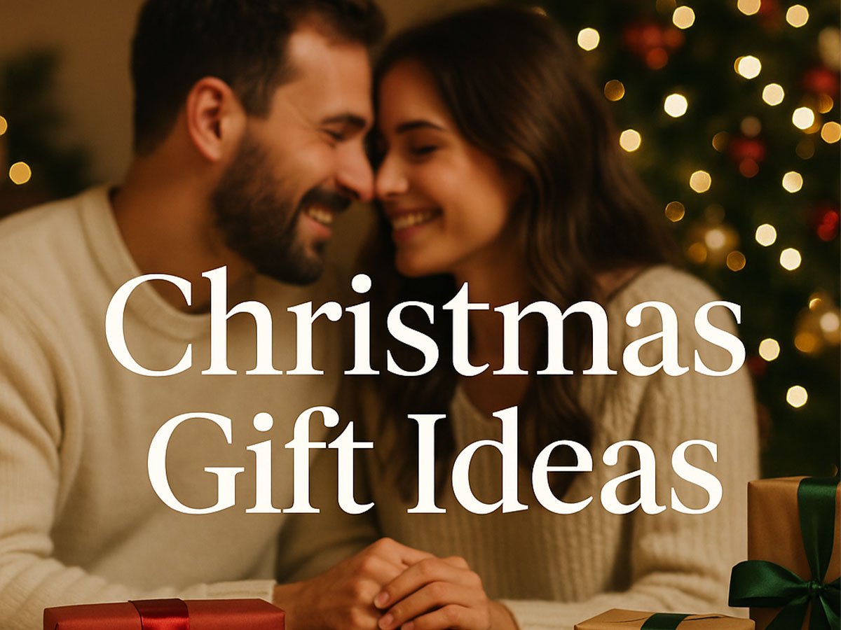 Smiling couple sitting together with wrapped Christmas gifts and warm holiday lights in the background.