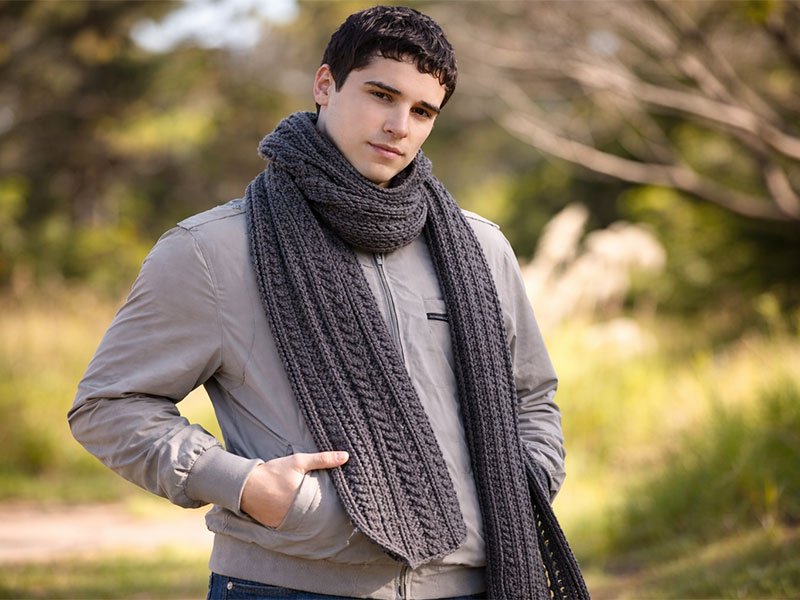 Man wearing a dark gray crochet scarf outdoors, styled with a casual jacket in cool weather.