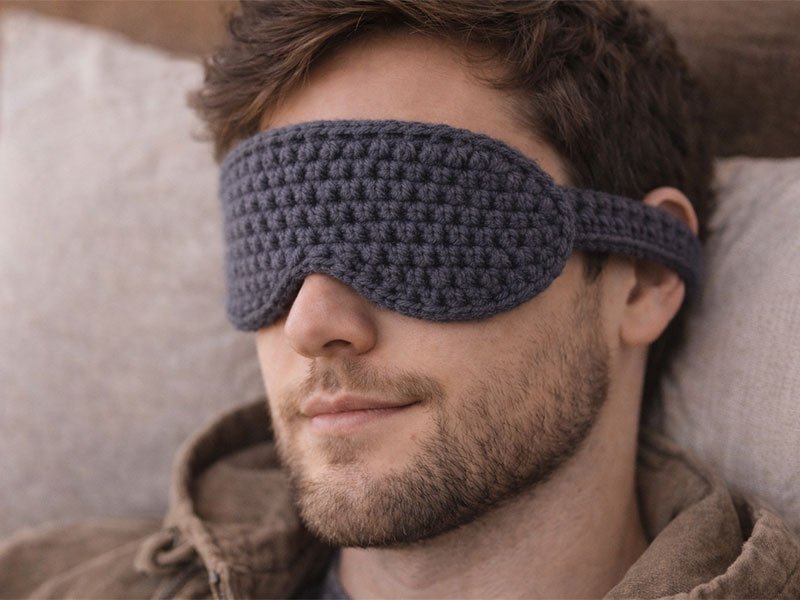 Man resting while wearing a soft gray crochet sleep mask for light blocking and comfort.