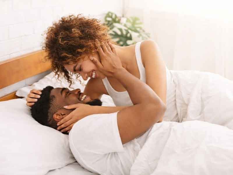 A joyful couple sharing a loving moment in bed, smiling and gazing into each other's eyes.