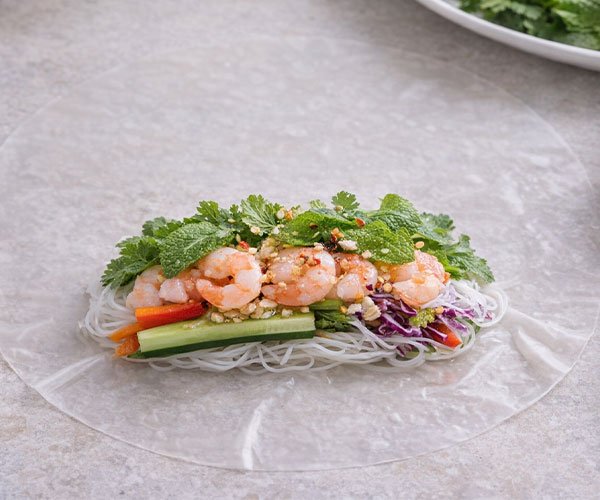 Rice paper wrapper with noodles, shrimp, and vegetables placed in the center ready for rolling.
