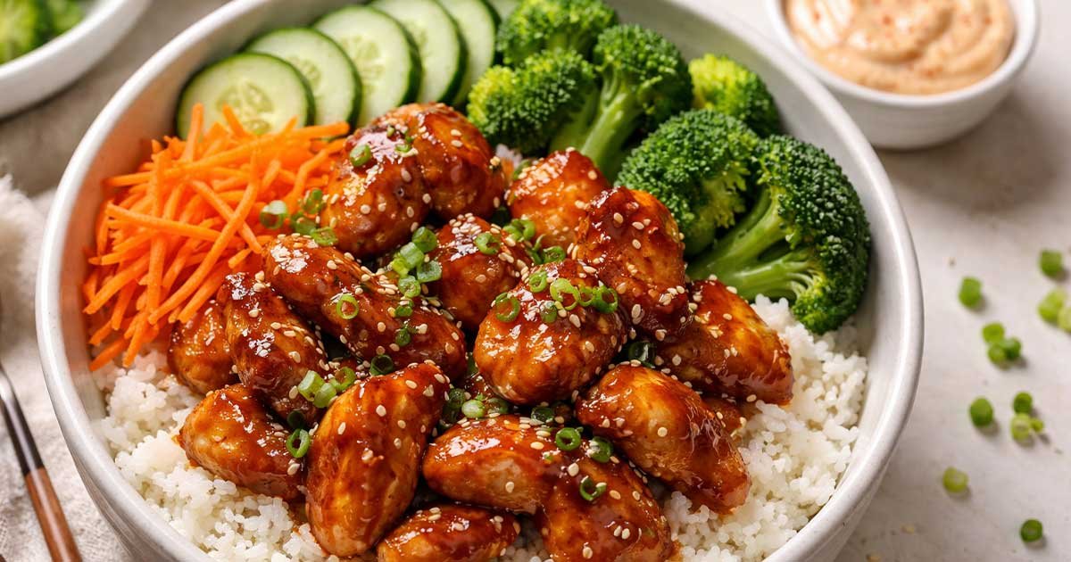 Sticky chicken bowl with glazed chicken over rice, served with broccoli, cucumber slices, and shredded carrots.
