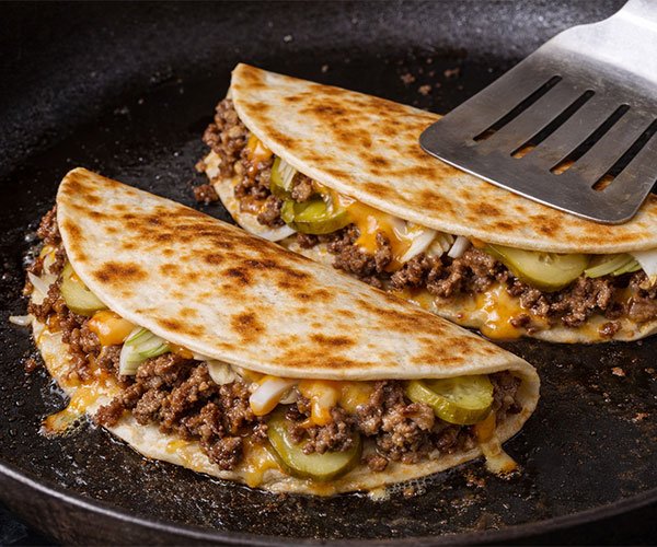 Smashburger quesadilla folded and pressed in a skillet with melted cheese, ground beef, pickles, and onions.