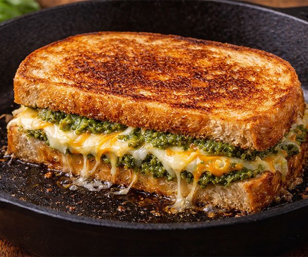 Golden sourdough pesto grilled cheese cooking in a cast iron skillet with melted mozzarella and cheddar