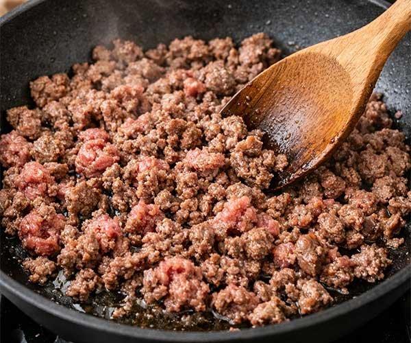 Ground beef browning in a skillet with a wooden spoon, cooking for a Korean ground beef bowl.