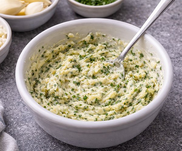 Bowl of creamy garlic herb butter mixed with minced garlic and parsley, ready to spread on bread for cheesy garlic bread.