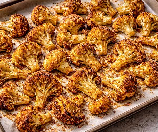 Moroccan-spiced cauliflower florets roasting on a parchment-lined baking sheet until golden, browned, and crisp around the edges.