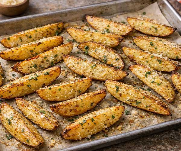 Garlic parmesan potato wedges baked until golden on a parchment-lined tray, sprinkled with herbs and cheese.
