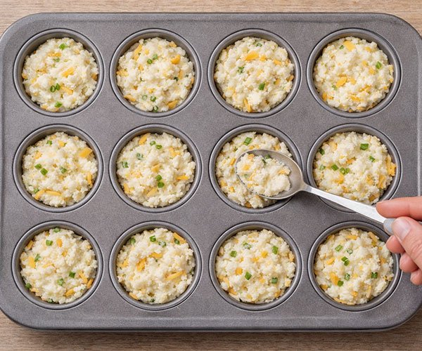 Spoon pressing mashed potato and cheese mixture into muffin pan cups, filled about three-quarters full.