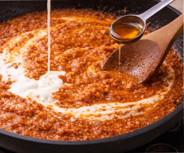 Cream being poured into a simmering butter chicken sauce while a spoon stirs it smooth and creamy.