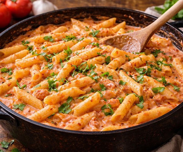 Penne pasta tossed in a creamy tomato garlic sauce in a skillet, topped with fresh parsley and ready to serve hot.