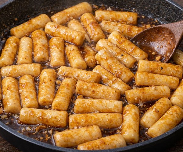 Korean rice cakes simmering in a thick soy butter sauce in a skillet