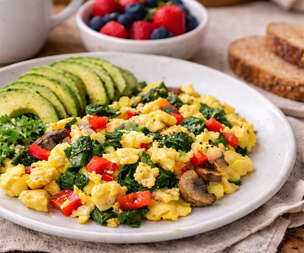 Veggie egg scramble with spinach, mushrooms, and red peppers served with sliced avocado, berries, coffee, and whole-grain toast.