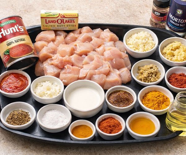 Ingredients for homemade butter chicken arranged on a tray, including diced chicken, tomato puree, butter, cream, oil, chopped onion, garlic, ginger, and assorted spices.