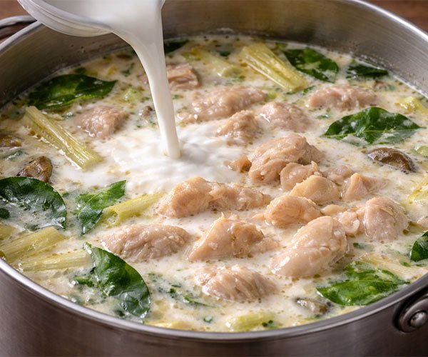 Adding coconut milk and chicken to Tom Kha Gai soup in a pot.
