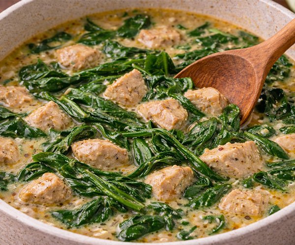 Adding vegetables to keto Thai curry chicken soup with spinach in creamy coconut broth.