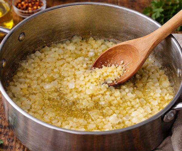 Chopped onions and minced garlic sautéing in olive oil or butter in a stainless steel pot with a wooden spoon.