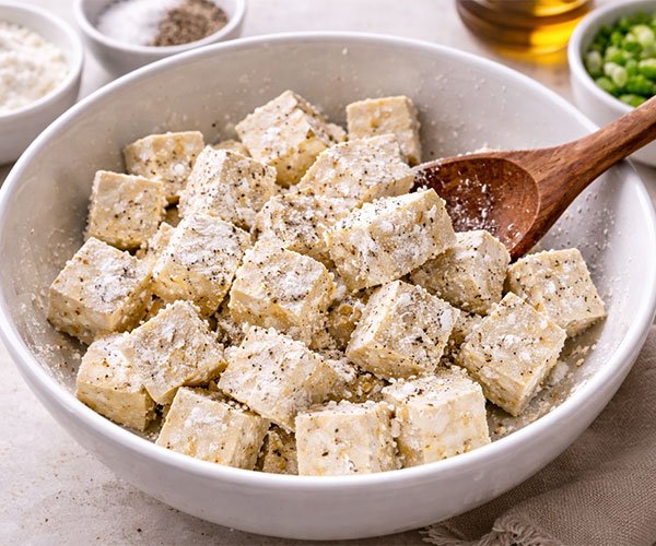 Tofu cubes coated with cornstarch, salt, and black pepper in a mixing bowl.