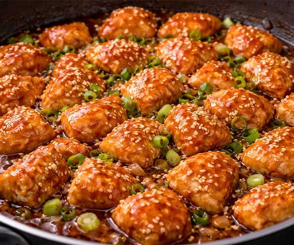 Cooked chicken simmering in honey sesame sauce in a pan.