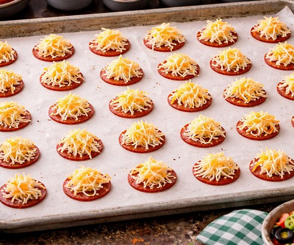 Pepperoni slices topped with shredded cheese arranged on a baking tray.