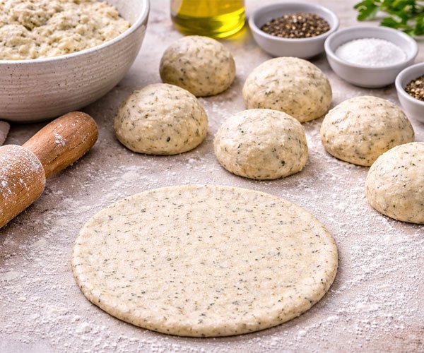 Cottage cheese flatbread dough divided into balls and one rolled flat on a floured surface with a rolling pin nearby.