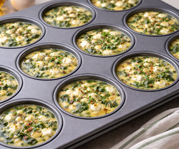 Egg and spinach mixture poured into a muffin tin, filling each cup for low-carb egg muffins.