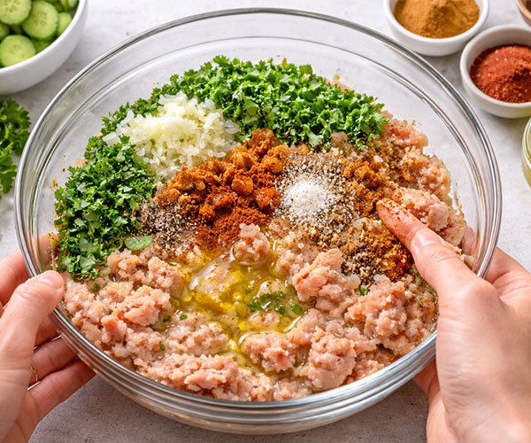 Mixing the chicken kofta base in a bowl with ground chicken, herbs, spices, onion, garlic, and olive oil.