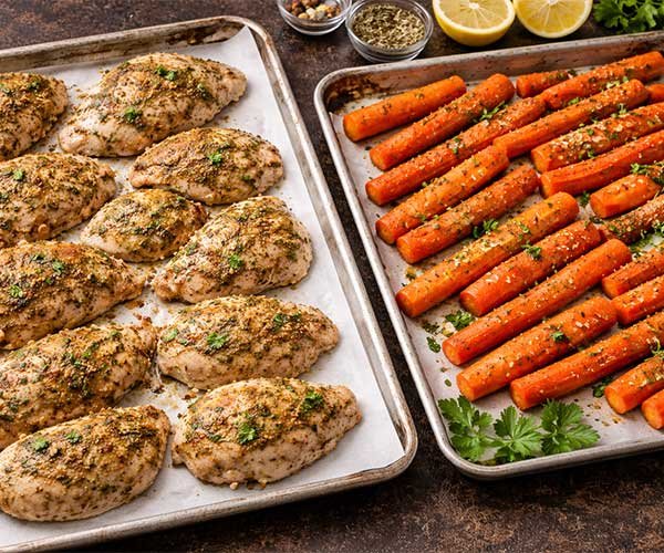 Seasoned chicken and carrots arranged on baking trays before roasting.