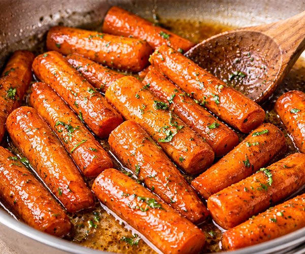 Glazed carrots cooking in butter and brown sugar in a skillet.