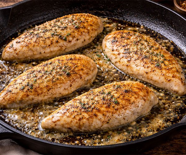 Chicken breasts searing in a hot skillet with butter and olive oil, developing a deep golden crust.