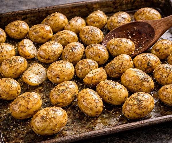 Seasoned baby potatoes coated with olive oil, oregano, salt, and black pepper on a baking tray