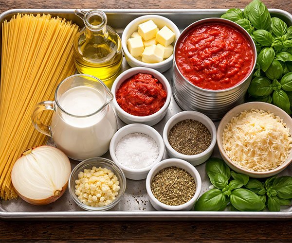 Ingredients for Tomato Garlic Pasta neatly arranged in a tray, including pasta, olive oil, butter, garlic, onion, tomato paste, crushed tomatoes, heavy cream, herbs, Parmesan, and fresh basil.
