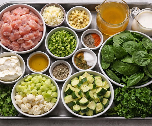 Tray of prepped keto soup ingredients with diced chicken, chopped veggies, greens, broth, cream, cream cheese, and spices.