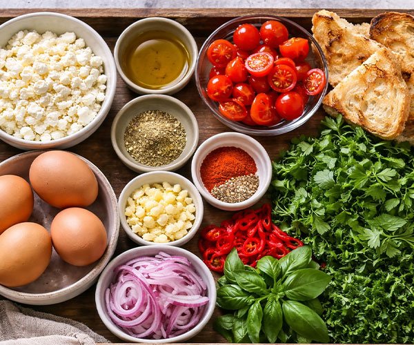 Tray with feta cheese, eggs, cherry tomatoes, herbs, spices, and bread neatly arranged.