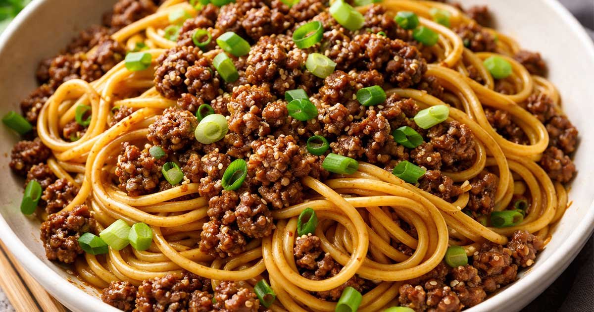 Bowl of Mongolian ground beef noodles topped with green onions and sesame seeds.