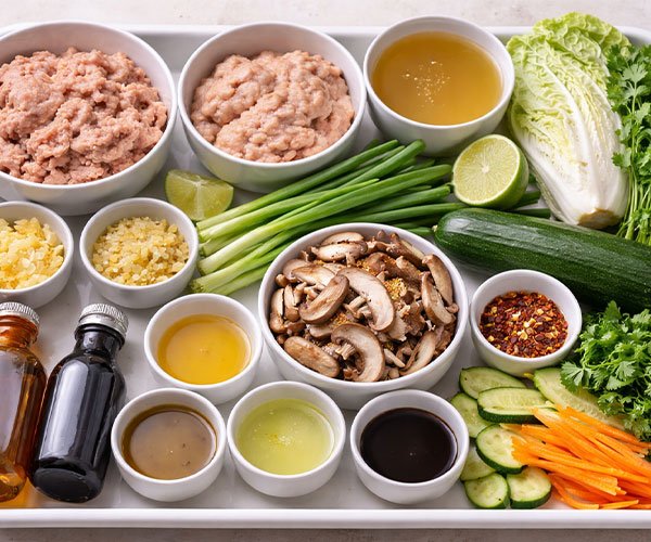 Tray with raw ingredients for potsticker soup including ground meat, vegetables, and seasonings.