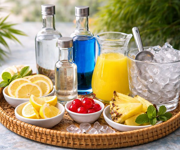 Cocktail ingredients including vodka, blue curaçao, pineapple juice, lemon, cherries, and ice arranged on tray.