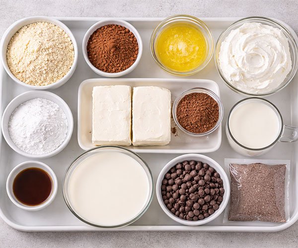 Tray with ingredients for low-carb chocolate lasagna including almond flour, cocoa powder, cream cheese, butter, almond milk, and chocolate chips.